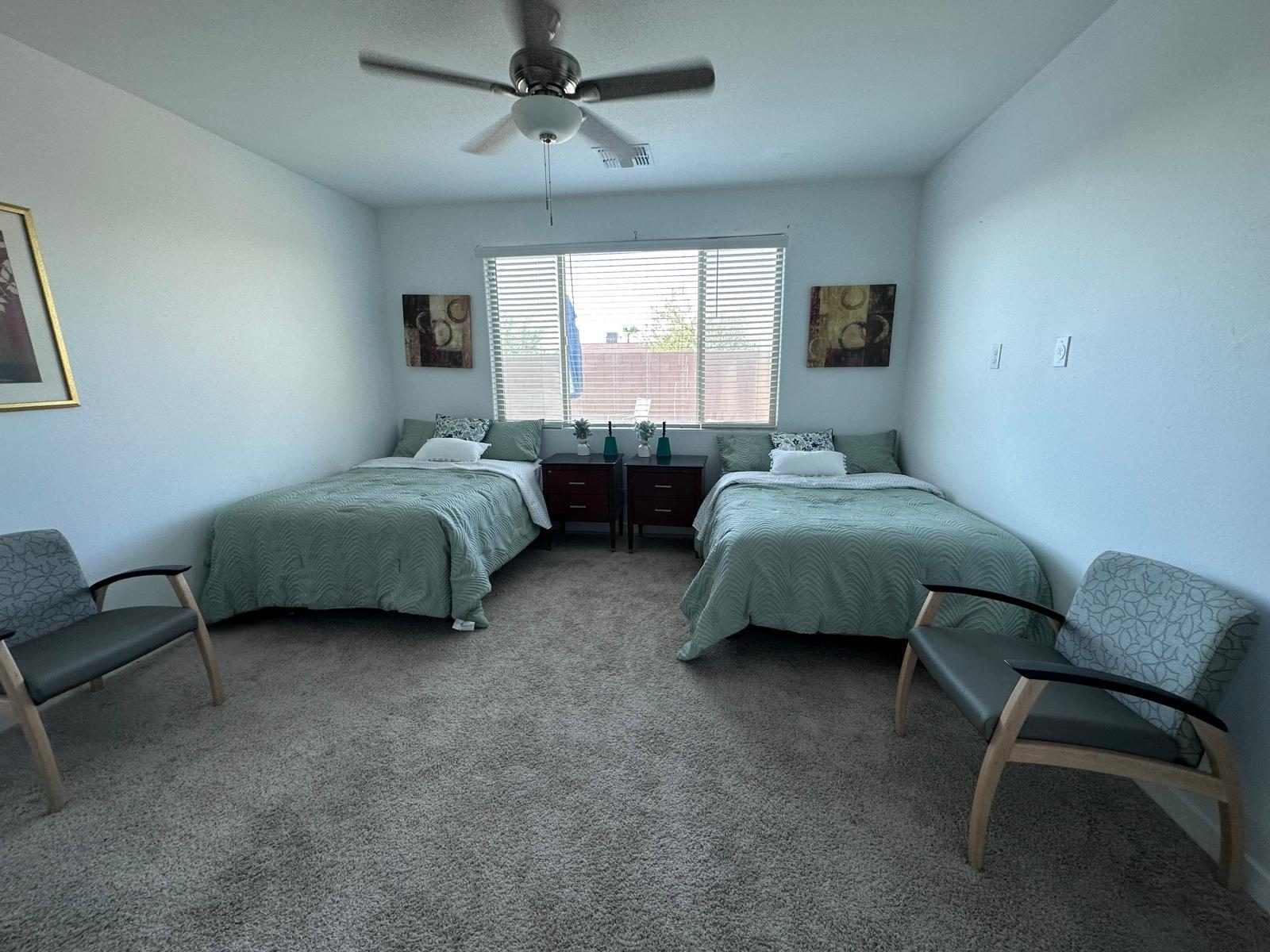 A shared bedroom for two adolescent residents, with sage-green bedding and natural light
